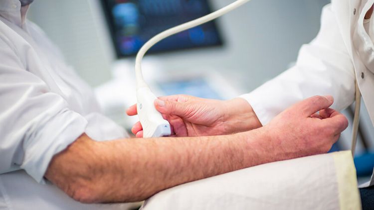 Arzt untersucht Arm eines Patienten mit Ultraschall