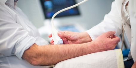 Arzt untersucht Arm eines Patienten mit Ultraschall